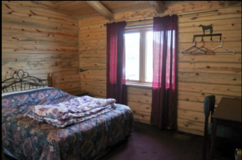 Cozy cabin bedroom with a wooden wall, a bed with a floral blanket, and a window with burgundy curtains.