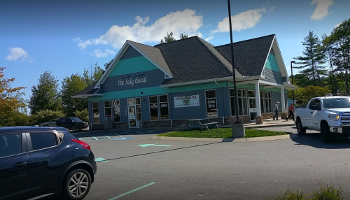 A modern building with a teal and gray exterior, featuring large windows and a "Now Hiring" sign.