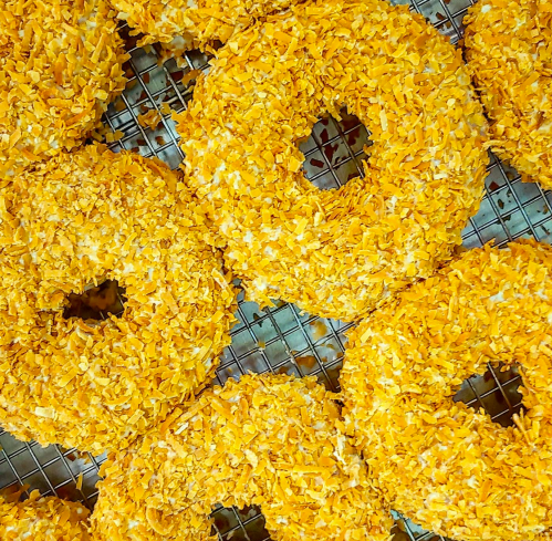 A close-up of golden donuts coated in crunchy orange flakes, arranged on a wire rack.