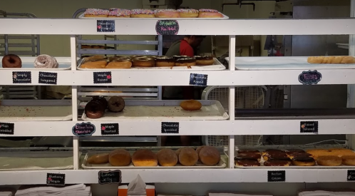 A display of assorted donuts on shelves, featuring various flavors and toppings in a bakery setting.