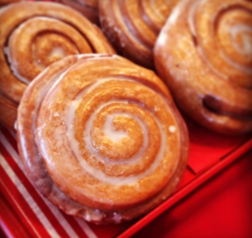 Close-up of glazed cinnamon rolls arranged on a red tray, showcasing their spiral shape and shiny icing.