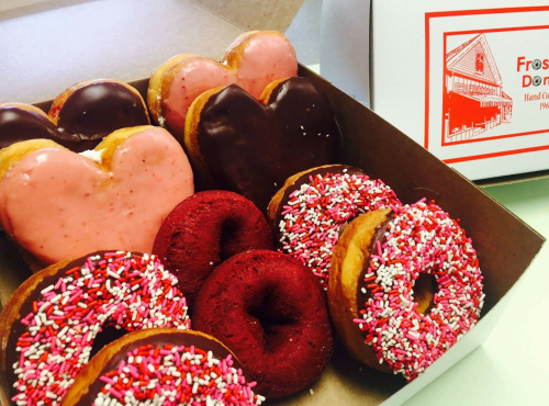 A box of assorted donuts, including heart-shaped, chocolate-covered, and red velvet with sprinkles.