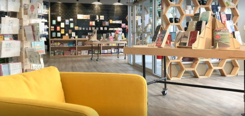 A cozy bookstore interior featuring a yellow couch, wooden shelves, and a variety of books on display.