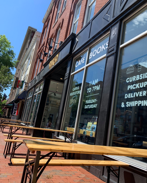 A sunny street view of a café and bookstore with outdoor seating, featuring large windows and an open sign.