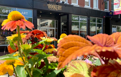 A vibrant flower bed in front of a café and bookstore called "Bookery," with colorful blooms and a welcoming entrance.