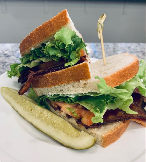A stacked sandwich with lettuce, tomato, and bacon, served with a pickle on the side.