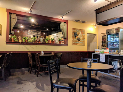 Cozy restaurant interior with black tables and chairs, plants, and a decorative rooster painting on the wall.