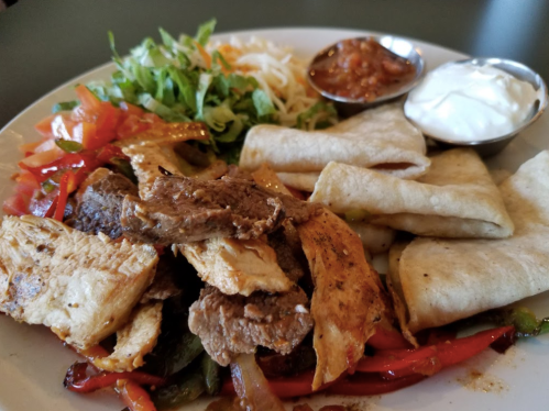 A plate of grilled meats, tortillas, lettuce, cheese, salsa, and sour cream, showcasing a colorful Mexican meal.