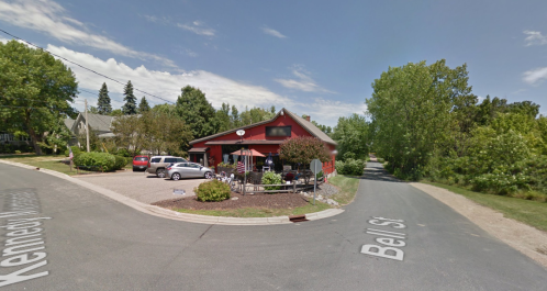 A red building at the corner of Kennedy Avenue and Bell Street, surrounded by trees and parked cars.