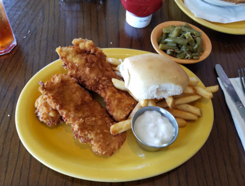 A plate with two fried fish fillets, fries, a roll, and a small cup of dipping sauce, with green beans on the side.