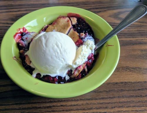 A green bowl filled with berry cobbler topped with a scoop of vanilla ice cream and a silver spoon.