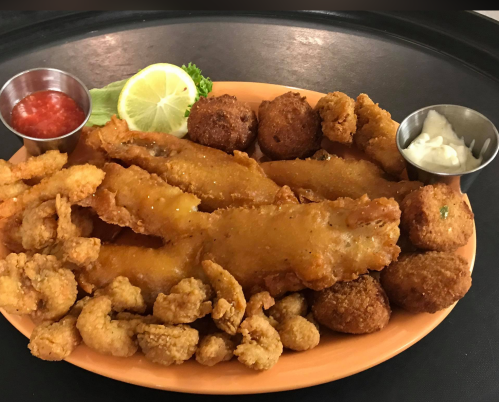 A platter of fried seafood including shrimp, fish fillets, and hushpuppies, served with lemon and dipping sauces.
