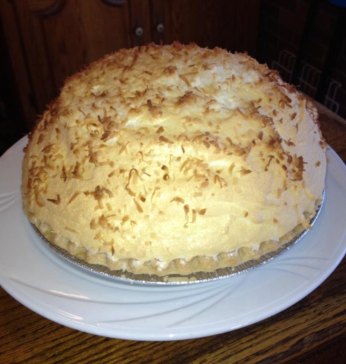 A round coconut cream pie topped with toasted coconut flakes on a white plate.