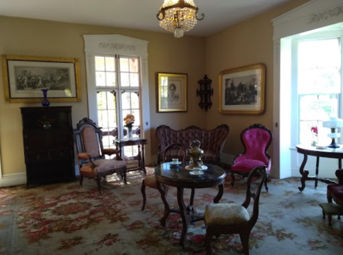 A vintage living room with ornate furniture, a chandelier, and framed artwork on the walls.