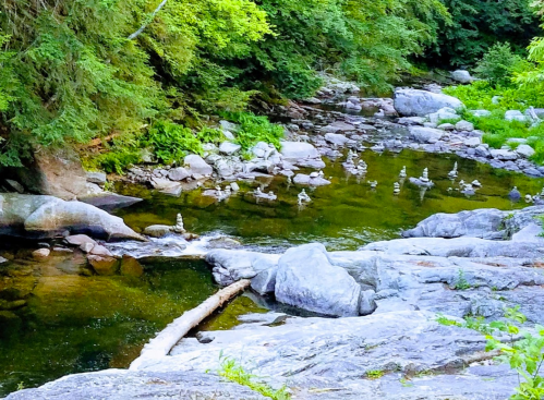 A serene river flows through a rocky landscape, surrounded by lush greenery and stacked stones along the water's edge.