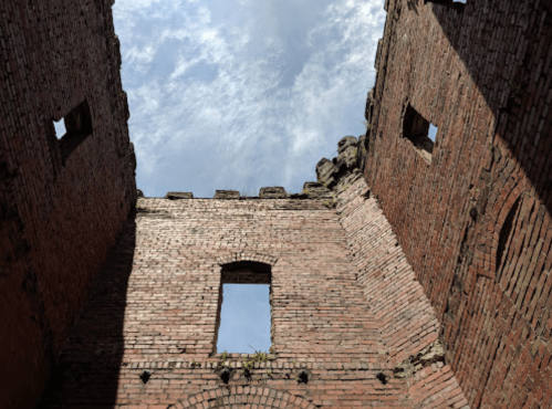 View looking up at the sky through the ruins of a brick structure with windows and crumbling walls.