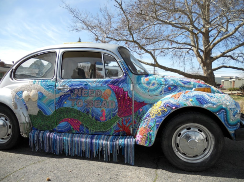 A colorful, beaded Volkswagen Beetle decorated with vibrant patterns and the words "NEED TO BEAD."
