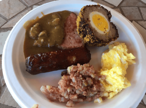 A plate of food featuring sausage, ham, a scotch egg, scrambled eggs, and a savory meat mixture.