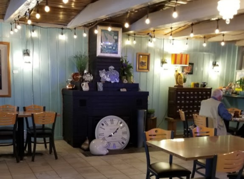 Cozy café interior with wooden beams, string lights, a decorative fireplace, and tables set for dining.