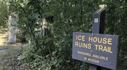 A wooden sign reading "Ice House Ruins Trail" stands among greenery, with stone ruins partially visible in the background.