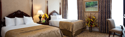 A cozy hotel room with two beds, elegant decor, a lamp, and a chair, featuring floral arrangements and a window view.