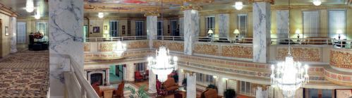 Elegant hotel lobby featuring marble columns, ornate gold detailing, chandeliers, and plush seating areas.