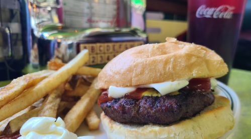 A juicy hamburger with ketchup and mayonnaise, served with crispy fries and a glass of Coca-Cola in a diner setting.