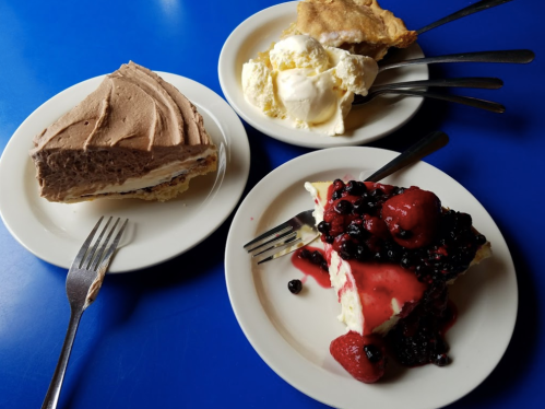 Three dessert plates: a slice of chocolate cream pie, a scoop of vanilla ice cream, and a berry-topped cheesecake.