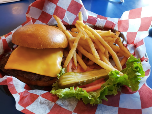 A cheeseburger with a melted slice of cheese, served with fries, lettuce, tomato, and a pickle on a checkered plate.