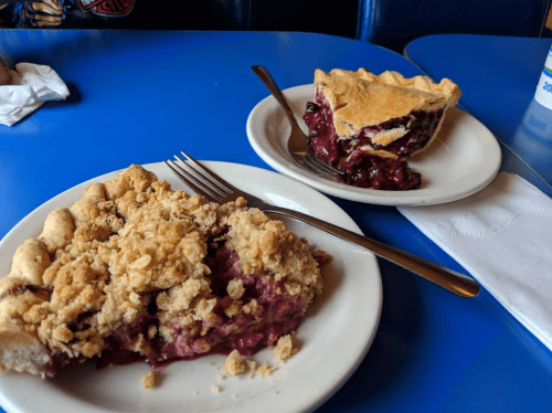 Two slices of pie on plates: one with a crumb topping and the other with a golden crust, set on a blue table.