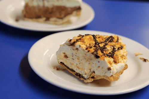 A slice of dessert with a creamy filling and a crunchy topping on a white plate, set against a blue background.