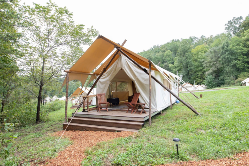 A glamping tent with wooden steps and chairs, surrounded by greenery and trees in a serene outdoor setting.