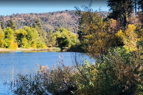 A serene lake surrounded by trees and mountains, with colorful autumn foliage reflecting in the water.