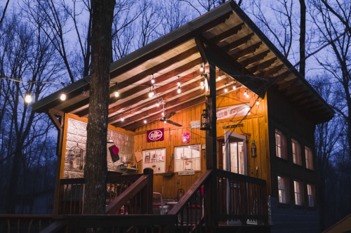 A cozy wooden cabin illuminated by string lights, surrounded by trees at dusk.
