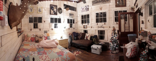 Cozy room with a patchwork bedspread, a couch, holiday decor, and rustic wooden walls adorned with various decorations.