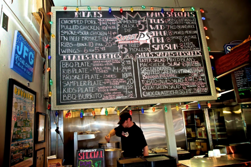 Chalkboard menu featuring meats, daily specials, and prices in a vibrant restaurant setting with festive lights.