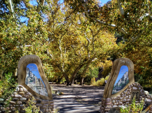 Two stone archways with maps welcome visitors to a colorful, tree-lined canyon path in autumn.