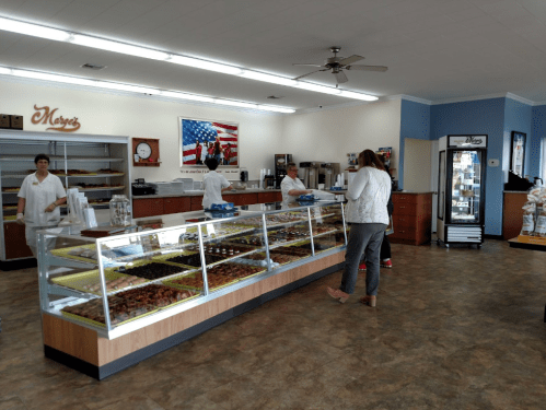 A bakery interior with a display case of pastries, staff behind the counter, and customers browsing in a bright space.