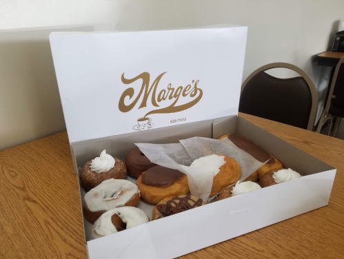 A box of assorted donuts, including frosted and cream-filled varieties, on a wooden table.