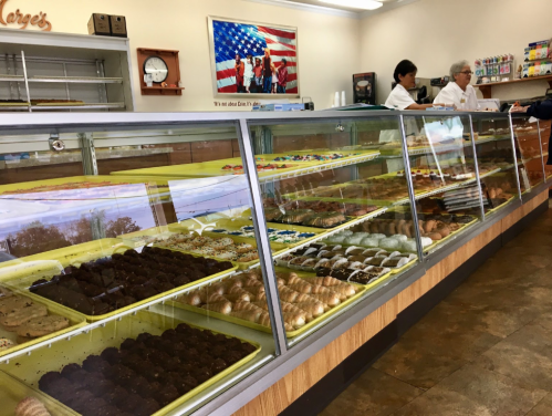 A bakery display case filled with various pastries and cookies, with staff serving customers in the background.