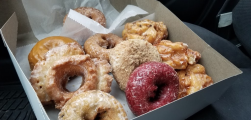 A box of assorted donuts, including glazed, cinnamon, and red velvet varieties, sitting in a car.