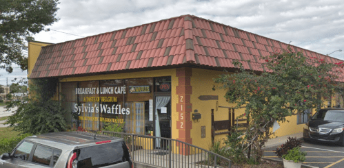 Exterior of Sylvia's Waffles cafe, featuring a red-tiled roof and large windows with signage for breakfast and lunch.