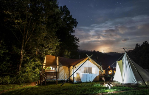 A serene campsite at night with tents under a starry sky and a glowing moon peeking through the clouds.