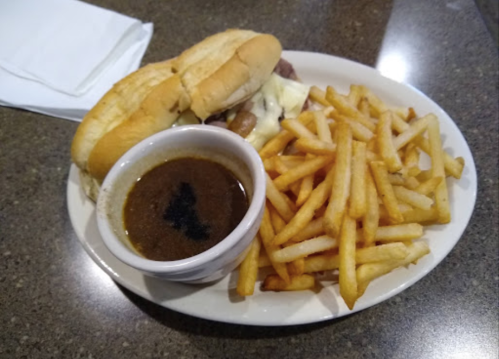 A plate with two sandwiches, a bowl of gravy, and a side of golden French fries on a dark table.