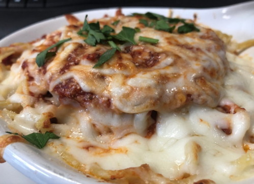 A close-up of a cheesy pasta dish topped with marinara sauce and fresh parsley in a white bowl.