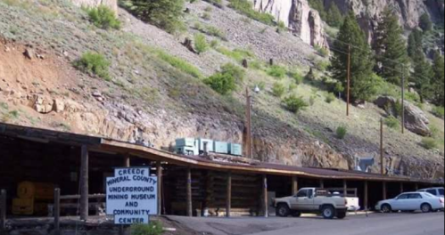 A rustic building at the base of a mountain, featuring a sign for the Creede Underground Mining Museum and Community Center.