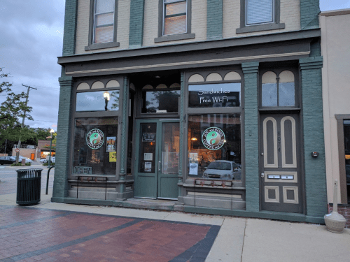 A quaint sandwich shop with large windows, offering free Wi-Fi, located in a brick building on a city street.