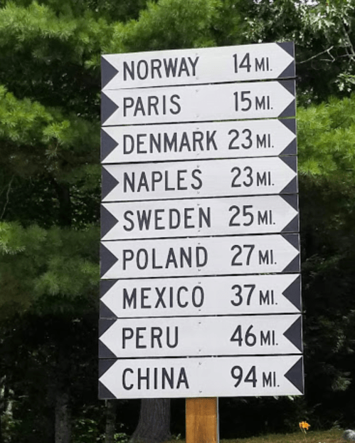 Signpost with directional arrows and distances to various locations: Norway, Paris, Denmark, Naples, Sweden, Poland, Mexico, Peru, China.