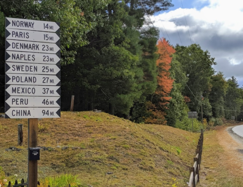 Signpost indicating distances to various locations: Norway 14 mi, Paris 15 mi, Denmark 23 mi, and more.