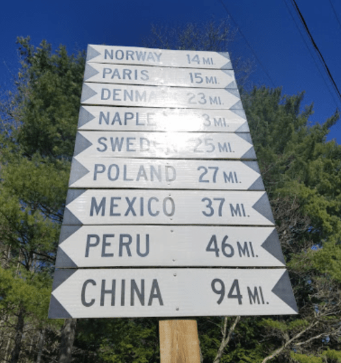 Signpost displaying distances to various locations: Norway, Paris, Denmark, Naples, Sweden, Poland, Mexico, Peru, and China.
